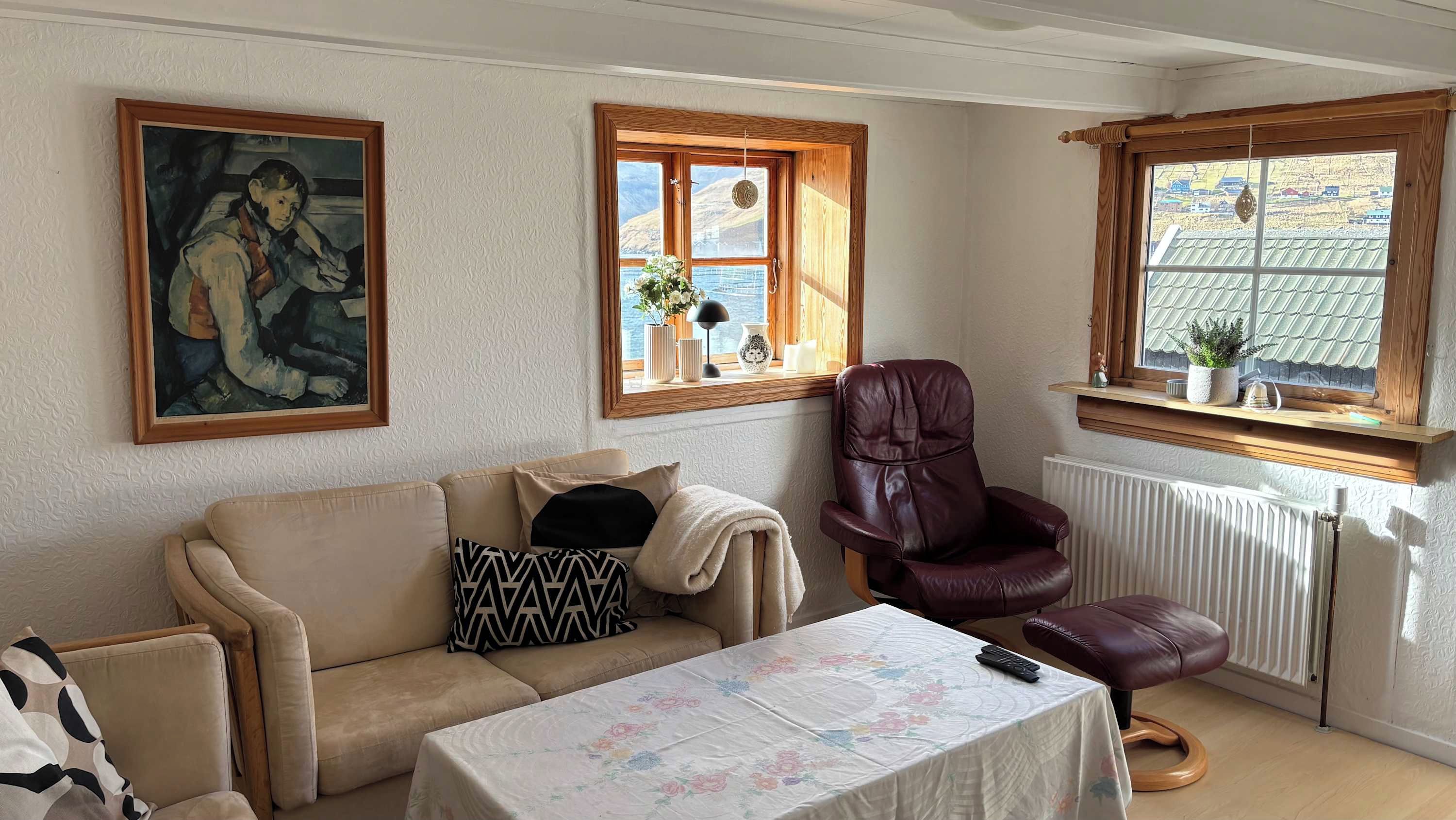 Ein gemütliches Wohnzimmer mit einer Couch, einem Ledersessel, einem Tisch mit Blumenmuster und einem Bild an der Wand.