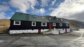 A black and white building with a red door, stone foundation, and a metal roof.