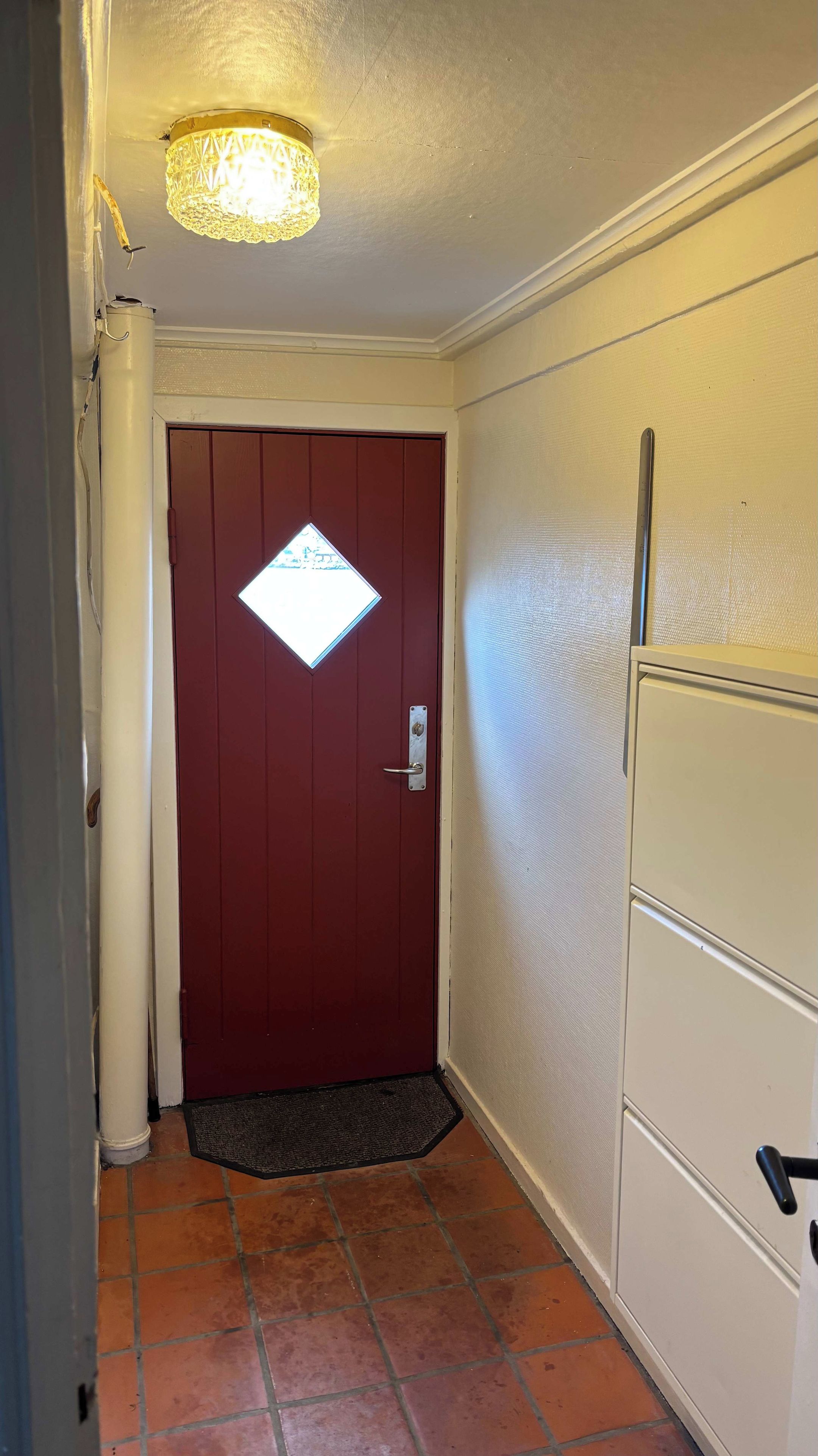 A hallway with a red door, a white radiator, and a tiled floor.