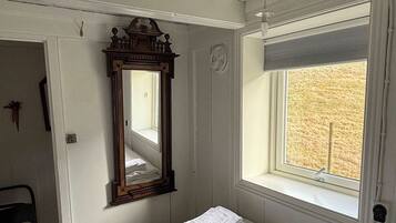 A room with a bed, a window with blinds, a ceiling fan, and a wall-mounted mirror.