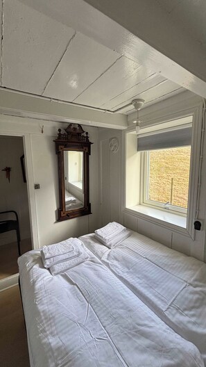 A room with a bed, a window with blinds, a ceiling fan, and a wall-mounted mirror.