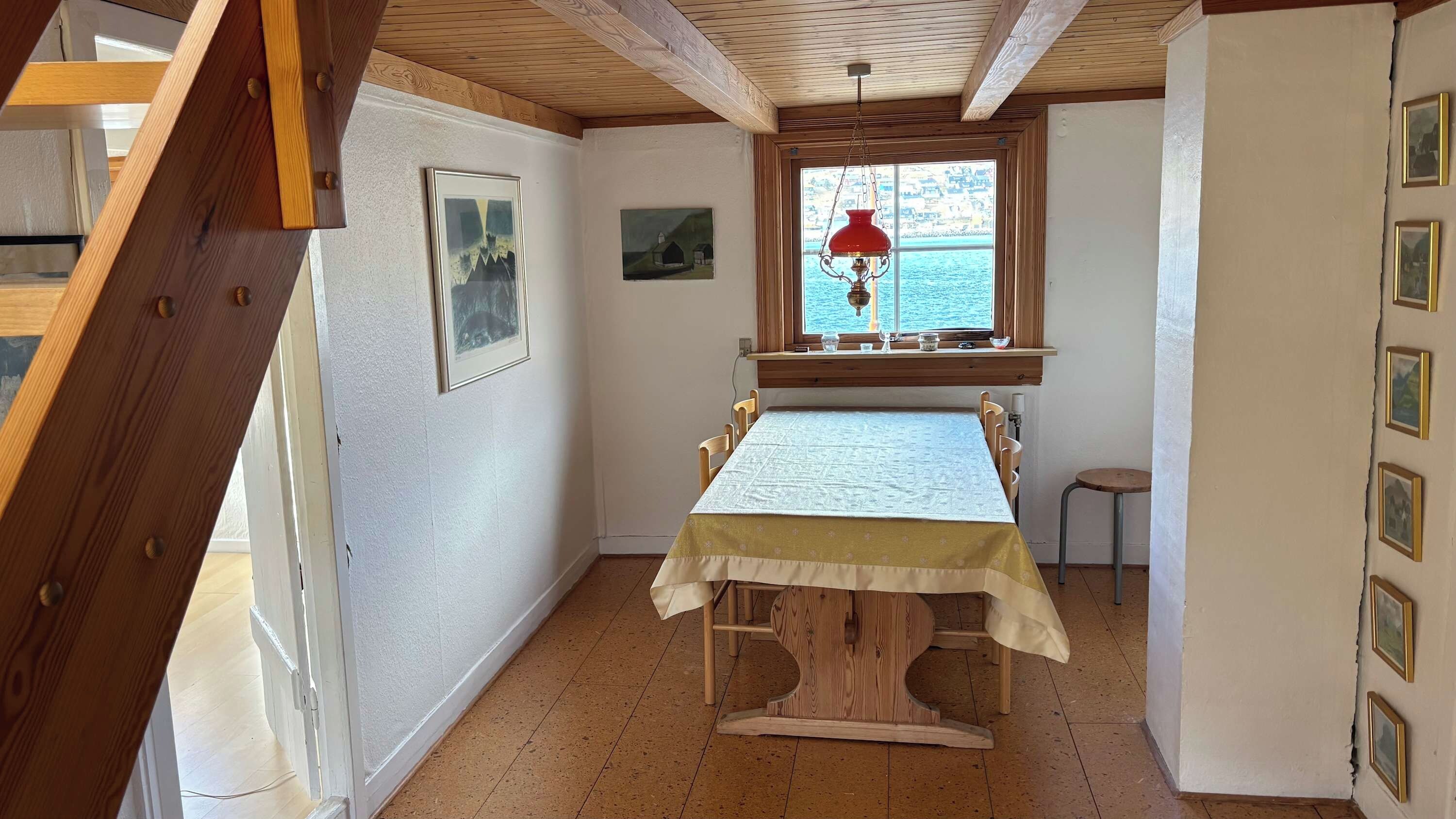 Un comedor con una mesa dispuesta para cuatro, una ventana con vista al mar y vigas de madera en el techo.
