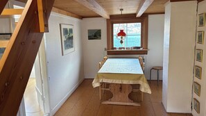 A dining area with a table set for four, a window with a view of the sea, and wooden beams on the ceiling.