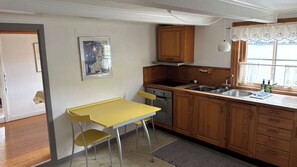 A compact kitchen with wooden cabinets, a yellow table, and a window with curtains.