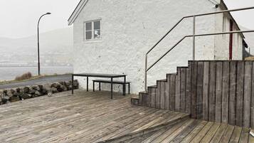 A wooden deck leading to a white building with a window and a bench.