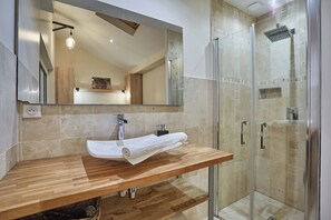 Ein modernes Badezimmer mit einem Holzwaschtisch, einem großen Spiegel, einer Duschkabine aus Glas und einem Handtuch auf der Ablagefläche.