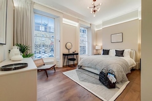 Ein Hotelzimmer mit Bett, Nachttisch, Stuhl und Blick auf die Stadt durch große Fenster.