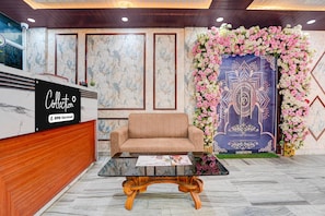 A reception area with a marble wall, a sofa, a wooden reception desk, and a floral wall decoration. - Classic Hotel Dream Palace (Danapur)