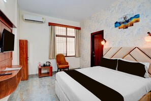 A hotel room with a bed, a TV, a chair, a small table, and a window with curtains.