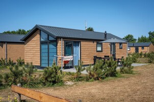 A modern wooden cabin with a large window, a door, and a small outdoor seating area.