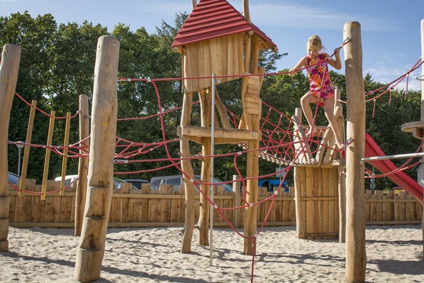 A wooden play structure with a rope net and a small red-roofed tower.