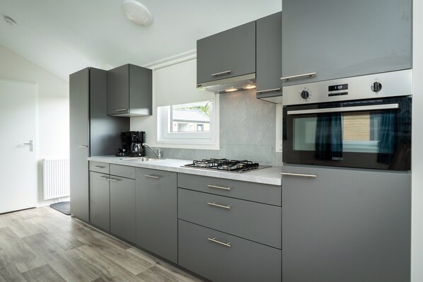 Une cuisine moderne avec des meubles de couleur grise, un four encastré et une cuisinière à gaz.