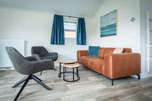 A modern living room with a grey armchair, a brown sofa, and two round wooden tables.