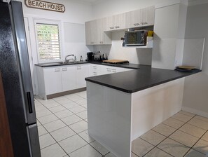 A kitchen with white cabinets, a black countertop, and a sign that reads 'BEACH HOUSE'. - Villa 36 - Tangalooma - Moreton Island (moreton island)