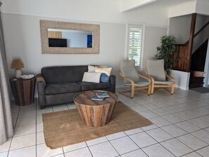 A living room with a sofa, a round coffee table, a chair, a lamp, and a mirror on the wall. - Villa 36 - Tangalooma - Moreton Island (moreton island)