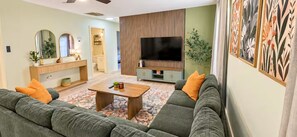 A living room with a sofa set, a coffee table, a TV, and a decorative wall. - Modern 2BR Retreat/ Sleeps 6/ Near Downtown (Spartanburg)