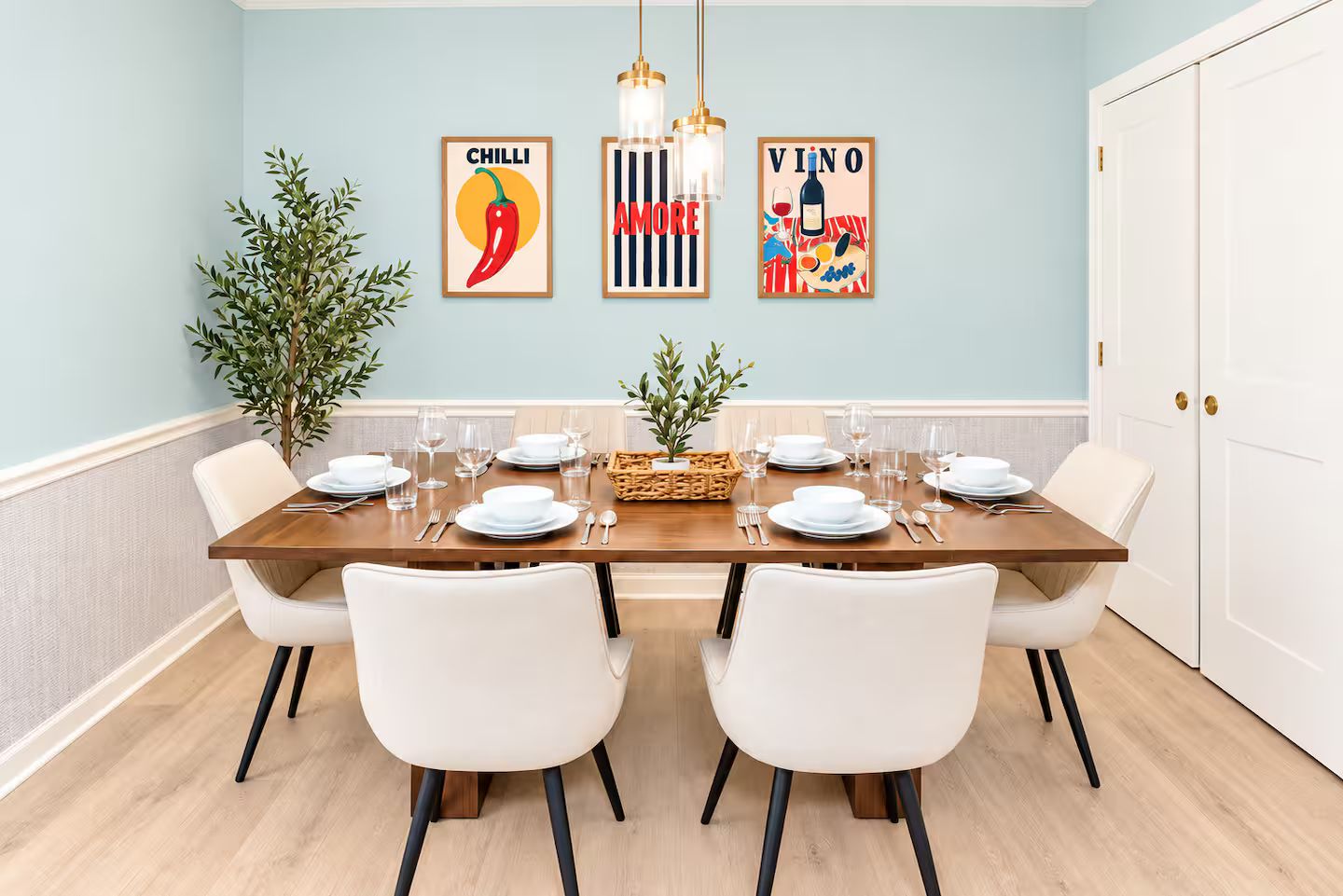 A dining room with a wooden table set for six, white chairs, and wall art depicting food and drink.