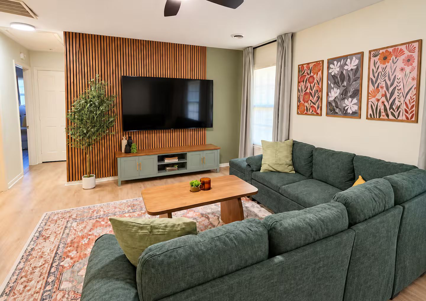 A modern living room with a sectional sofa, a flat-screen TV, a wooden accent wall, and a large window.