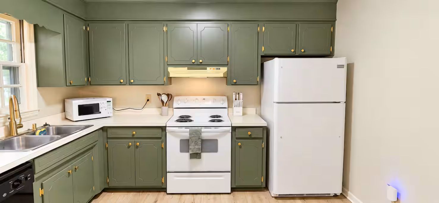 A kitchen with green cabinets, a white stove, a white microwave, and a white refrigerator.
