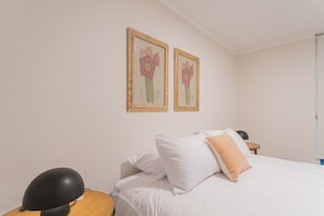 A hotel room with a bed, a nightstand, a lamp, and two framed floral pictures on the wall. - Santa Rosa Apartments by Andes (Santiago)