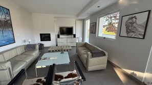 Un salon moderne avec un téléviseur à écran plat, deux canapés, une table basse et des œuvres d’art accrochées aux murs.