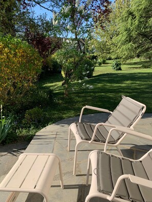 Eine Terrassenfläche mit zwei Lounge-Stühlen und einem kleinen Tisch, umgeben von einem gepflegten Rasen und verschiedenen Sträuchern.