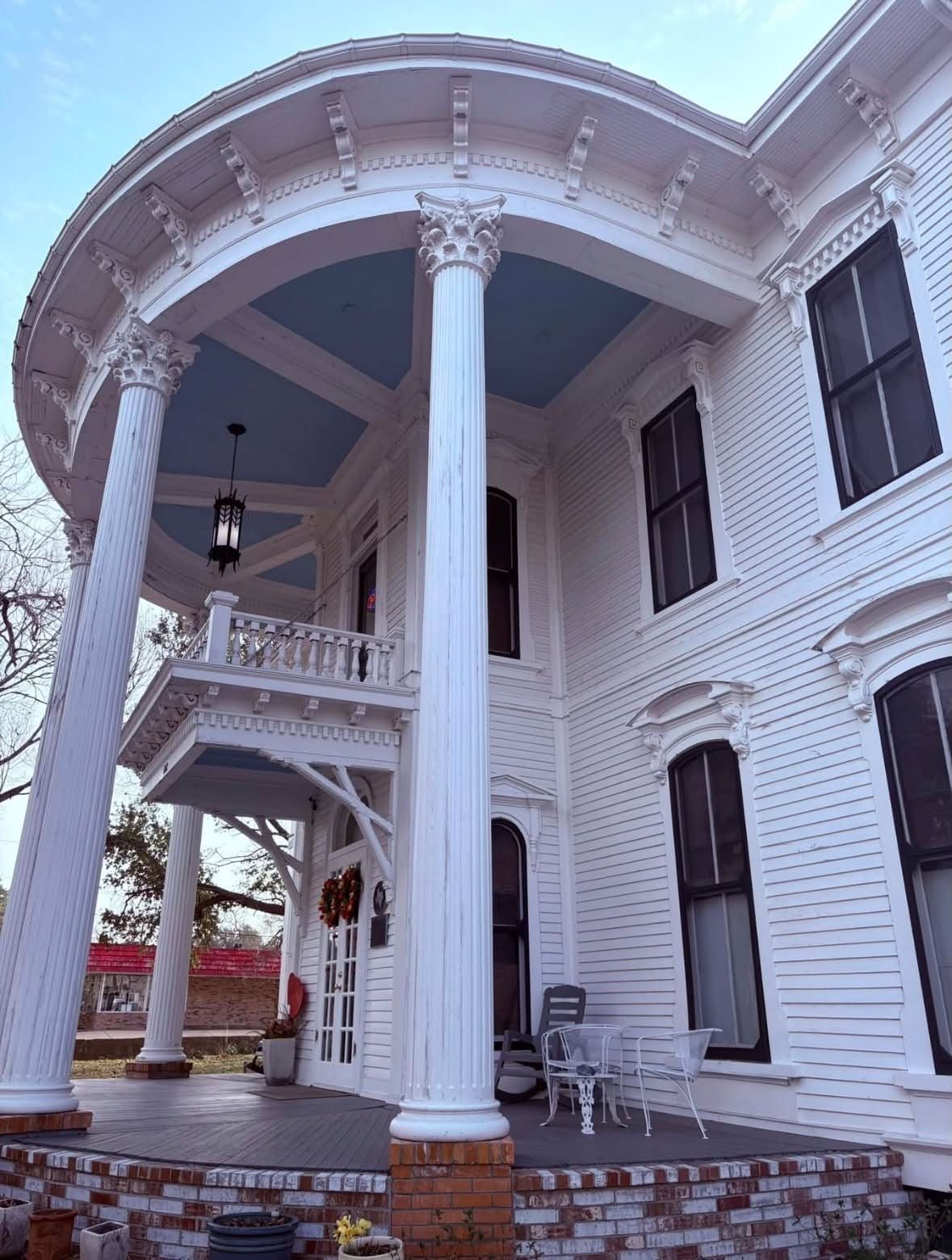 Un grand bâtiment blanc doté d’un porche couvert soutenu par des colonnes, avec un balcon et de nombreuses fenêtres.