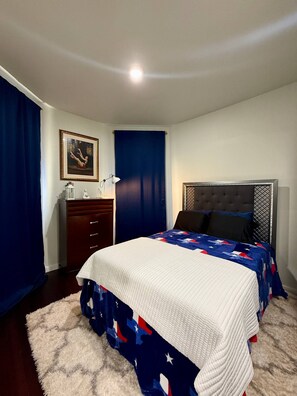 A bedroom with a bed, a dresser, a nightstand, a lamp, and a painting on the wall.
