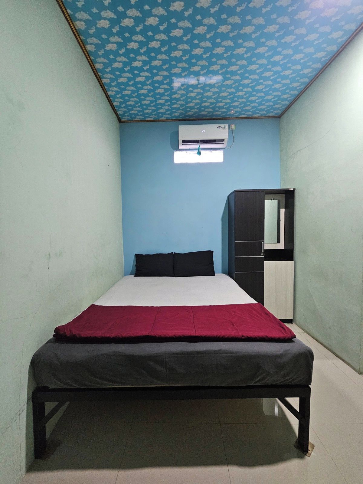 A bedroom with a bed, a wardrobe, and an air conditioning unit on the wall.