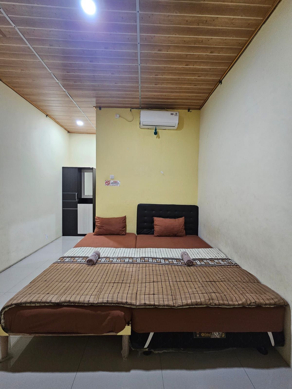 Habitación individual con una cama, techo de madera, aire acondicionado de pared y una pequeña kitchenette al fondo.