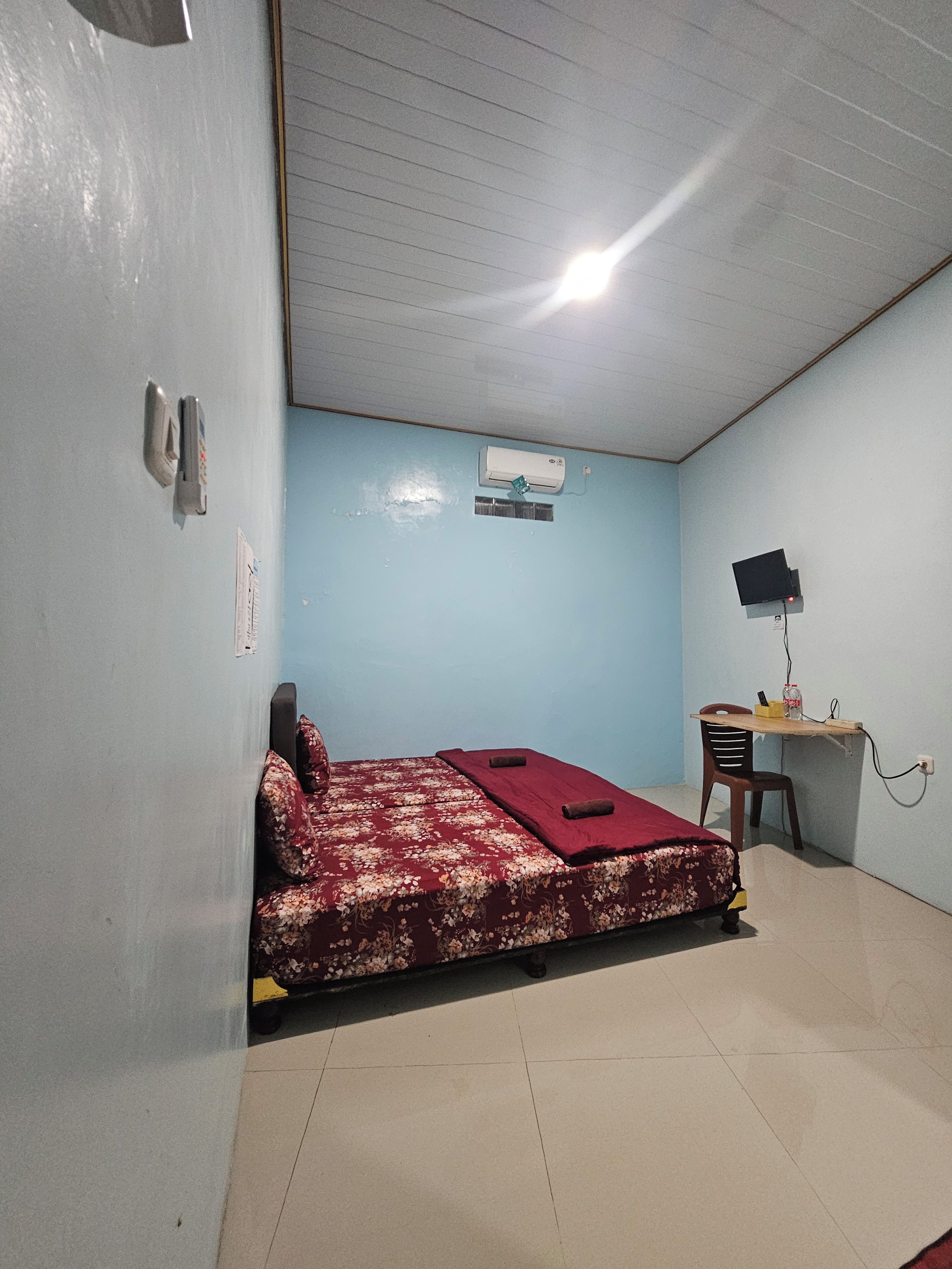 Una habitación con una cama, un escritorio con una silla, un aire acondicionado de pared y una lámpara en el techo.