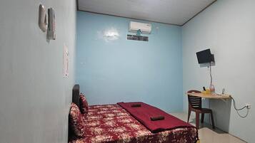 Una habitación con una cama, un escritorio con una silla, un aire acondicionado de pared y una lámpara en el techo.