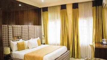 A hotel room with a large bed, a nightstand, a chair, and a desk with a cup.