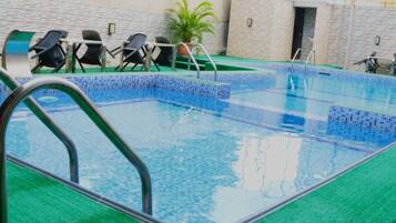 A swimming pool with a tiled edge, a metal ladder, and several chairs around the pool area.