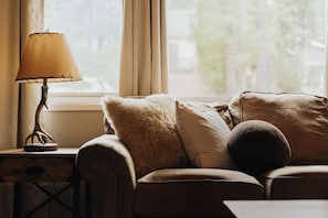 Um quarto aconchegante com um sofá, uma luminária e vista para o exterior.
