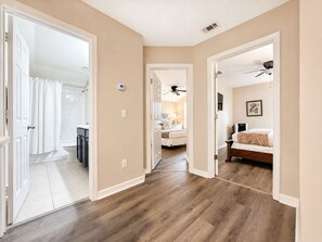 Um corredor com piso de madeira que leva a um quarto com cama e ventilador de teto.