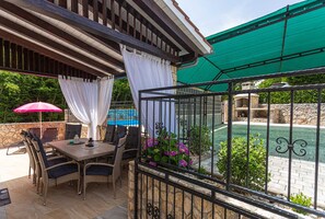 An outdoor patio with a table and chairs, a pool, and a stone wall. - Holiday apartment SANELA with private pool (Hlapa)