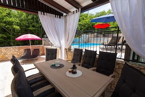 An outdoor patio with a table, chairs, and umbrellas, overlooking a swimming pool. - Holiday apartment SANELA with private pool (Hlapa)