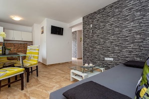 A modern living room with a sofa, a dining table with chairs, a kitchen area, and a stone-textured wall. - Holiday apartment SANELA with private pool (Hlapa)