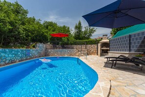 A swimming pool with a stone wall, a red umbrella, and a barbecue area. - Holiday apartment SANELA with private pool (Hlapa)