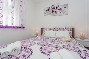 A neatly made bed with a patterned bedspread, two bedside lamps, a wall-mounted painting, and a window with curtains. - Holiday apartment SANELA with private pool (Hlapa)