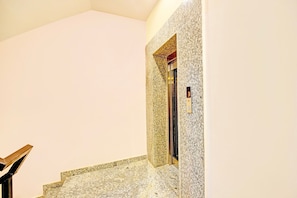 A staircase with a granite finish leading to an elevator. - Classic Charmwood Inn (Faridabad)