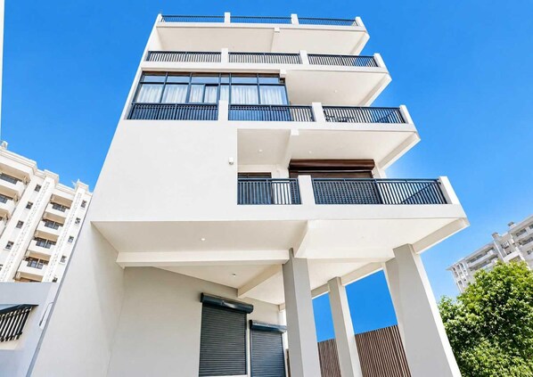A multi-story building with balconies, large windows, and a clear sky. - Classic Charmwood Inn (Faridabad)