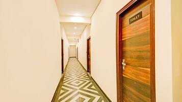 A hotel corridor with a geometric patterned floor, a wooden door labeled 'TOILET' on the right, and a hallway leading to a room.