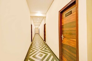 Un couloir d’hôtel avec un sol orné de motifs géométriques, une porte en bois portant l’inscription « TOILETTES » sur le côté droit, et un couloir menant à une chambre.