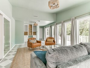 A spacious living area with a large sofa, two armchairs, and a coffee table. There is a view of a balcony through large windows. - Quail Creek Home | Koi Pond, 2 Kings, EV Charger (Oklahoma City)