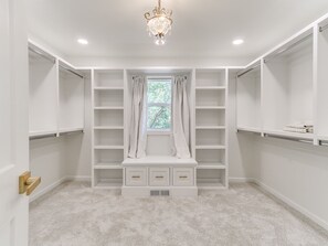 A walk-in closet with white shelving, a bench, and a chandelier. - Quail Creek Home | Koi Pond, 2 Kings, EV Charger (Oklahoma City)