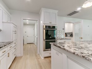 A modern kitchen with white cabinetry, a stainless steel oven, and a marble countertop. - Quail Creek Home | Koi Pond, 2 Kings, EV Charger (Oklahoma City)