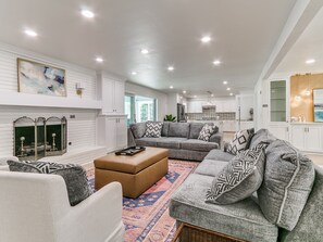 A spacious living room with a fireplace, a large grey sectional sofa, and a coffee table. - Quail Creek Home | Koi Pond, 2 Kings, EV Charger (Oklahoma City)
