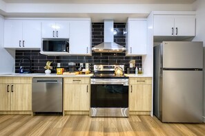 A modern kitchen with white cabinets, a stainless steel dishwasher, a built-in oven, and a refrigerator. - Welcome to Sapphire Inn which is 13  minutes from YYC Calgary Airport (Calgary)